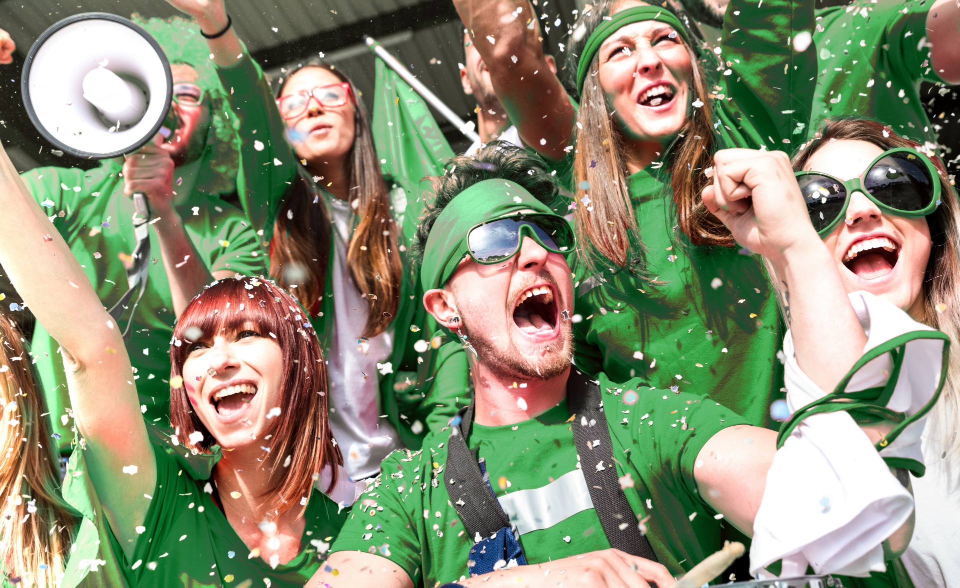 Young amateur football fan supporters cheering with confetti watching local soccer cup match at stadium - Friends people group on green t shirts having excited fun on sport world championship final